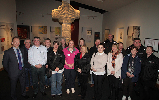 Members of Downpatrick Community Collective with guests and Mike King, Down County Museum Curator, pictured with the High Cross in the new display area.